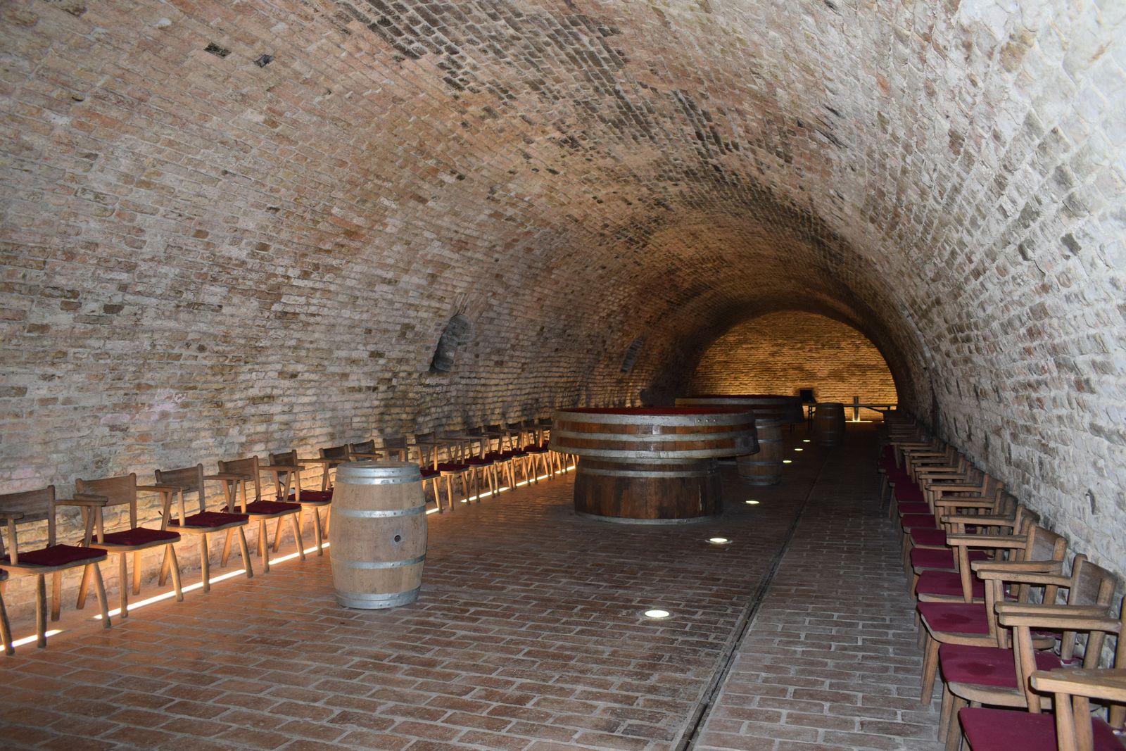 Explore a vintage brick wine cellar with wooden barrels and chairs in Kneževi Vinogradi, Croatia.
