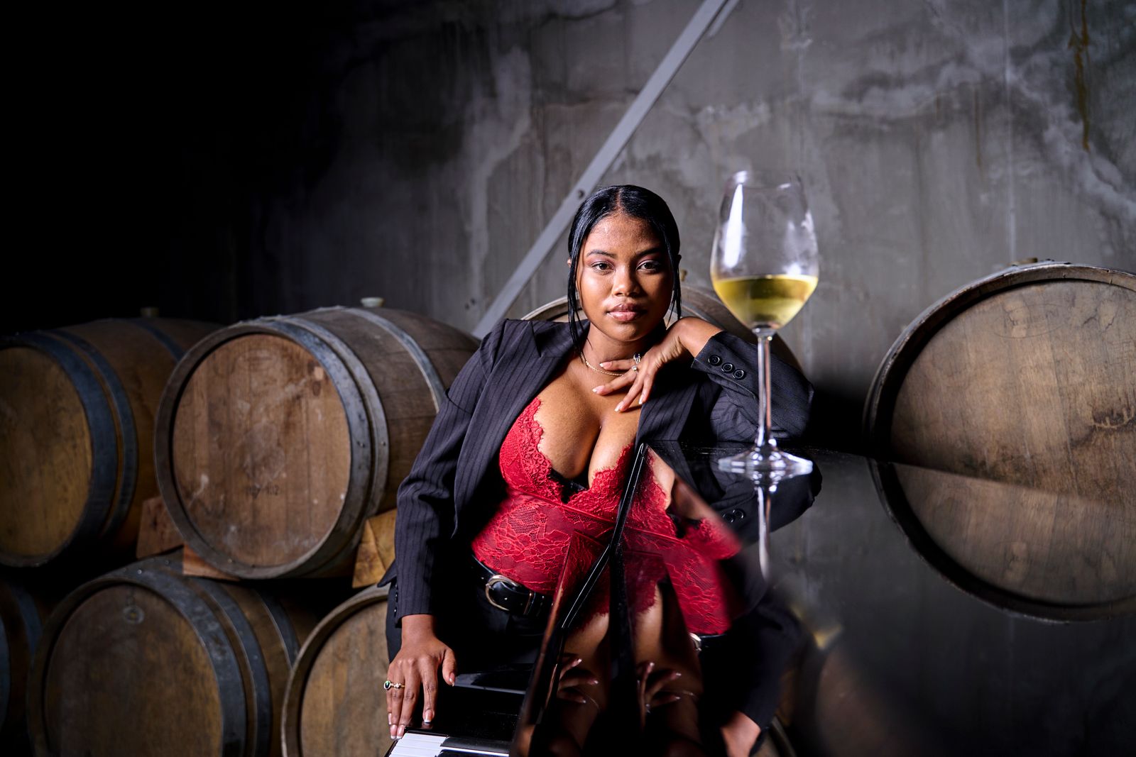 A stylish woman poses with a glass of wine in a rustic winery setting.