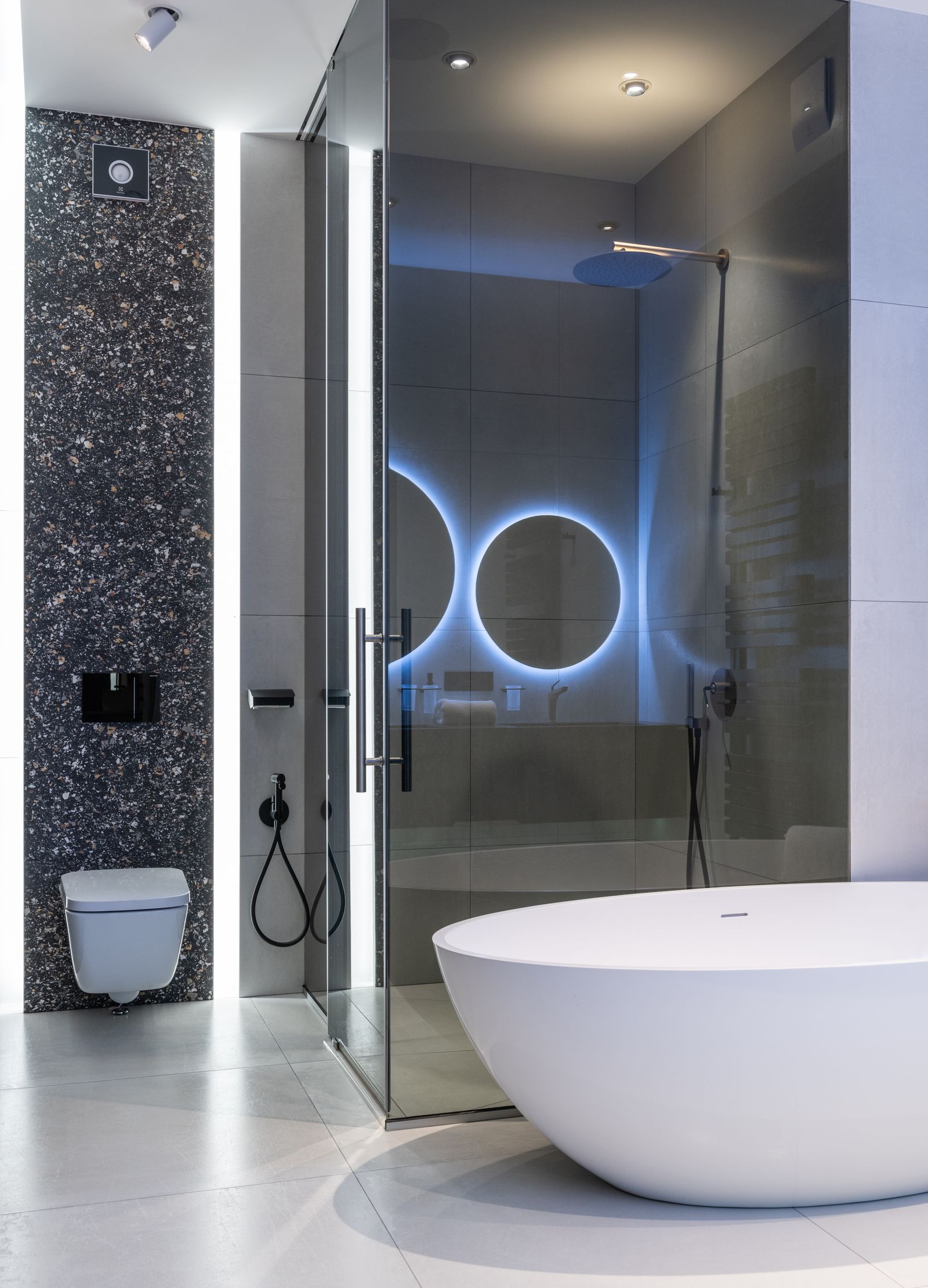 Stylish restroom with oval bathtub and toilet near glass shower with bright illumination